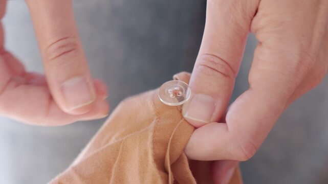 Closeup of woman fastening small buttons on brown fabric. Concept of clothing and textile care and everyday household routine