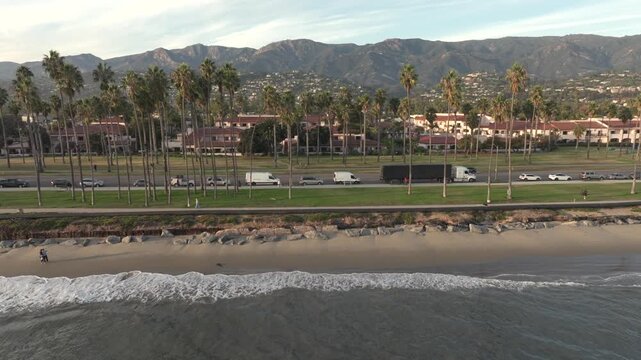 Santa Barbara, California, USA - Rightward Aerial View of East Beach With Chromatic Gate, People Running, Coastal Park and Mountain Range in Background at Sunset