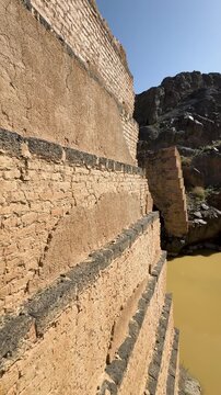 Muddy wadi water flowing past ancient dam ruins in a rocky Saudi Arabian canyon.