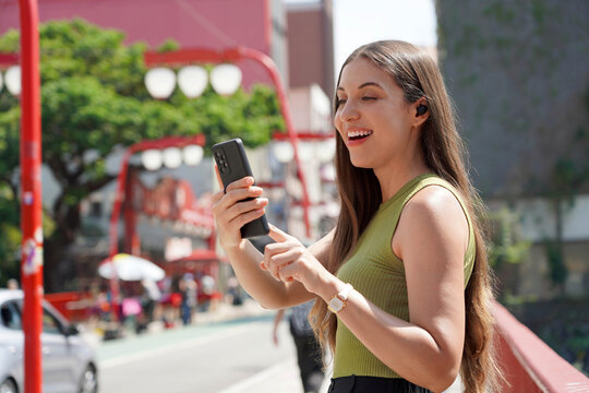 Beautiful Brazilian girl listening to music with earbuds and smartphone in Liberdade neighborhood of Sao Paulo, Brazil