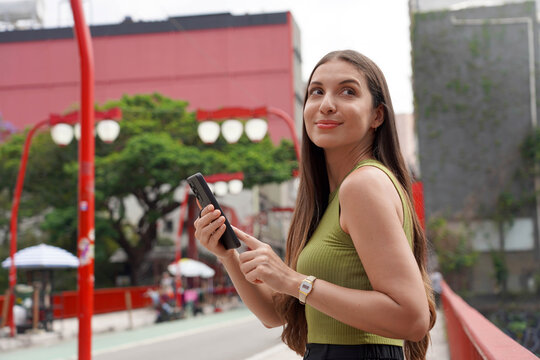Young tourist woman looks around using smartphone with ring holder to avoid phone theft in metropolis street center