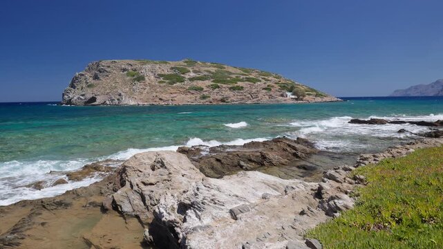 Static wide view of turquoise waves washing over coastal rocks, calm summer sea around Mochlos island in eastern Crete