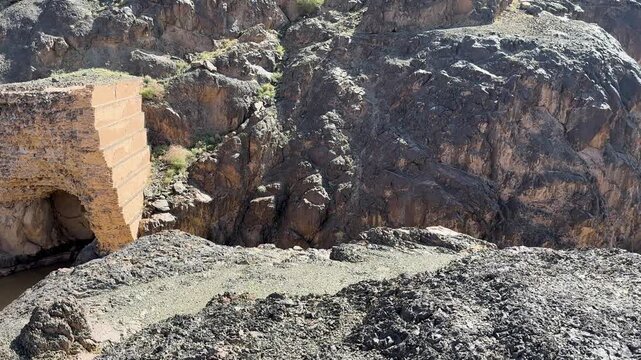 Historic dam ruins overlooking a vast rocky desert valley and muddy river in Saudi Arabia.