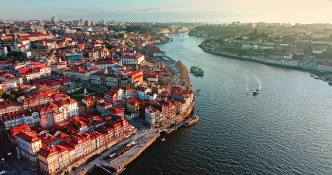Porto city aerial view panorama, historic Ribeira district and colorful buildings along the winding Douro River, with boats cruising on the water under a warm golden hour sky. Travel to Portugal