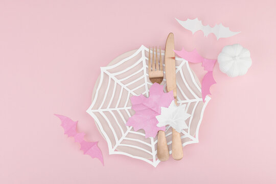 Pink Halloween table setting flat lay with plate, cutlery on rosy background