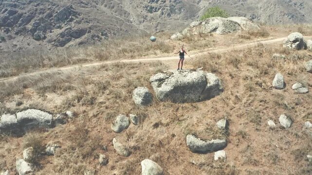 Happy woman throwing a ball in the air while standing on a rock in a vast, arid landscape