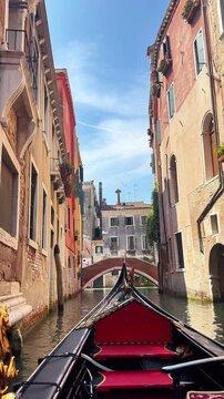 Tracking shot of gondola moving through narrow canal in Venice under blue sky