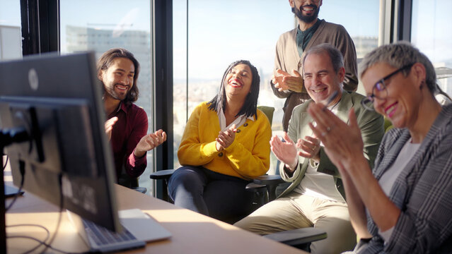 Diverse group of professionals applauding and celebrating together during an office meeting. Positive corporate scene conveying achievement, recognition, teamwork and shared success.