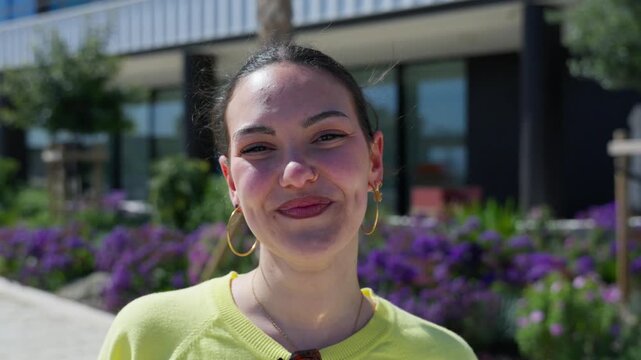 A happy young White woman without sunglasses walks toward the camera, laughing and making direct eye contact in bright sunlight.