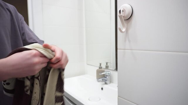 A man wipes his hands with a towel in the bathroom next to the sink and mirror. Light tiles, soap dispensers and a neat interior create a sense of cleanliness and everyday home care.