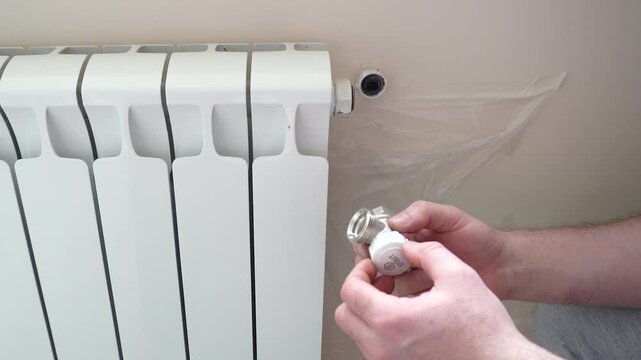 Installing the thermostat on the radiator. A man tries on a thermostat to a hole on a white radiator. The video demonstrates the process of preparing for the installation of the temperature controller