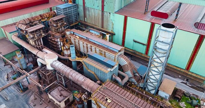 High angle view reveals complex industrial machinery, pipes, and smoke stacks at a modern manufacturing plant during daytime.