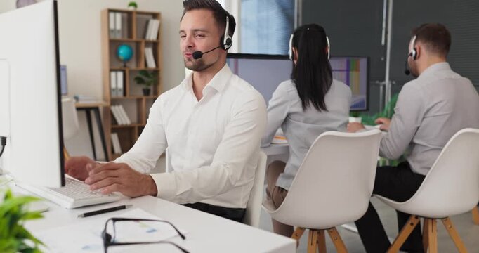 Agent operator answering call in center with headset. At a modern office the team provides customer service while working on computers and monitors. Clear customer support service concept.