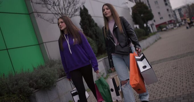 Two Teenage Girls Enjoy a Shopping Spree, Walking Down the Street with Colorful Shopping Bags and Sharing Laughter.