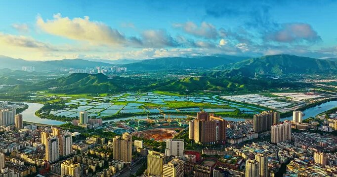 High-angle view showcases modern city skyscrapers, a winding river, and lush mountain ranges in Shenzhen under clear blue sky.