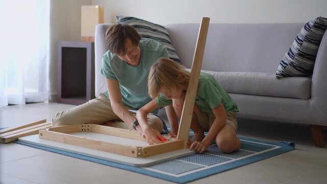 Father and ten-year-old son assembling wooden table on floor. Family teamwork.