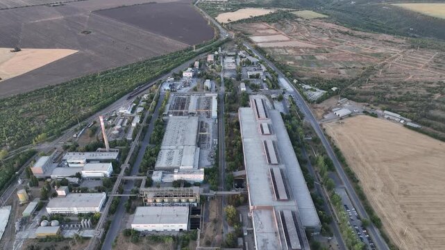 Steelmaking and rolling mill halls beside cultivated farmland in a drone aerial view. Heavy industry, regional development and industrial agricultural land use planning