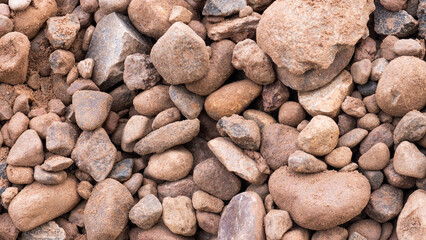 Close up of assorted river stones and pebbles covered with natural soil, forming rough earthy background with varied shapes, sizes, warm tones, and detailed surface patterns for nature design use. © bisonov