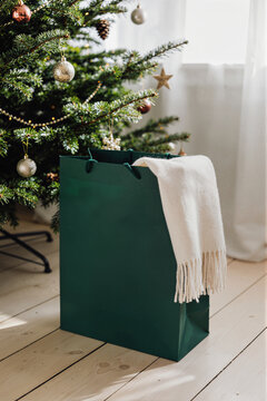 Green gift bag with knitted scarf beside decorated Christmas tree