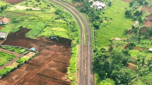 Aerial drone view of dual railway tracks passing through lush green agricultural fields and rural landscape