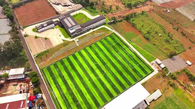 Aerial drone view of green soccer field and modern building near farmland