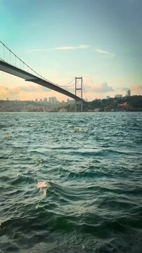 Scenic view of the Bosphorus Bridge in Istanbul with choppy sea waves and a motorboat cruising past.