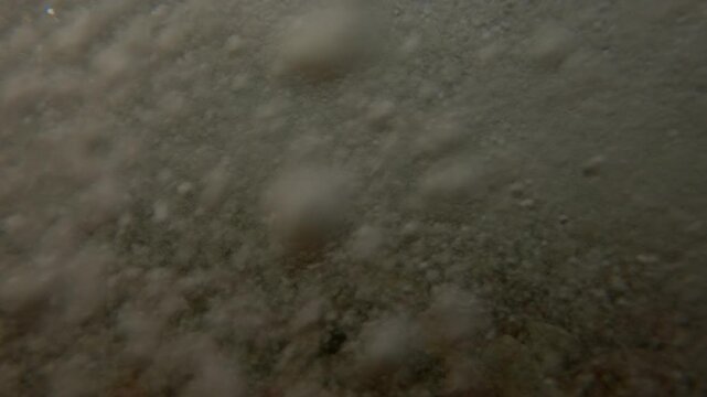 The waves are rolling and crashing on the pebble beach, Underwater view, Split level, Slow motion. Splashes and foam of sea waves and many air bubbles under the water surface