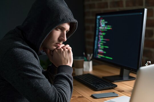 Hacker and coder working on software programming in a dark office at a computer desk monitor