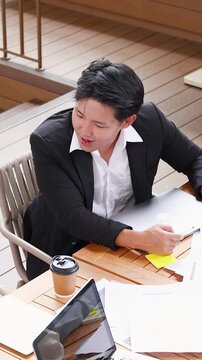 Frustrated Asian Businessman Discussing Work at Outdoor Cafe Table
