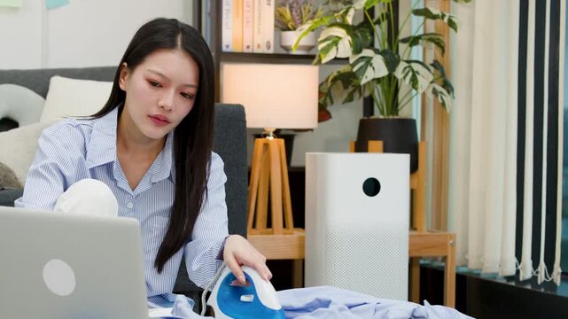 Asian Woman Multitasking by Ironing Clothes and Working on Laptop