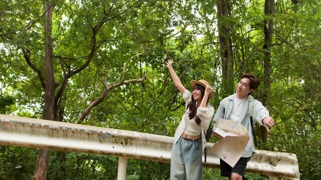 Young Couple Hitchhiking by Roadside Holding Map in Forest