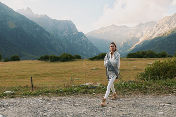 Obraz premium Young woman walks along a gravel road in a mountain valley, calm and thoughtful, framed by distant peaks, that suggest solitude, exploration, and a sense of open space.