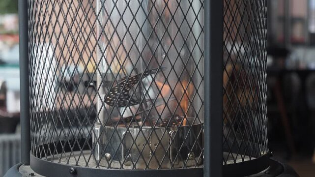 Outdoor patio heater burning bright orange flames inside glass tube with metal mesh guard.