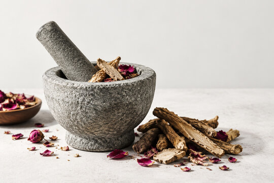 Stone mortar and pestle with dried mandrake roots and petals, herbal apothecary still life