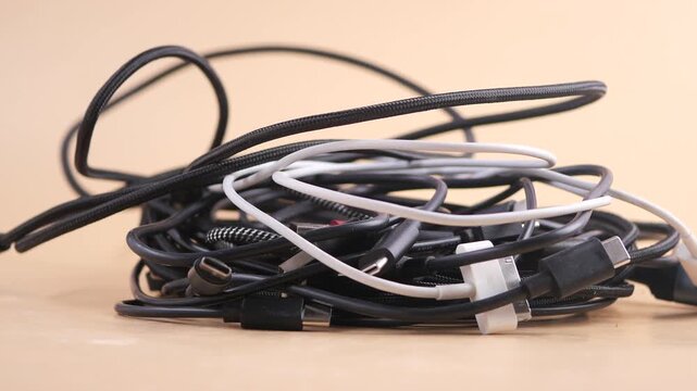 Close up view of tangled heap of black and white charging cables and data cords on light surface.