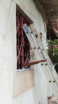 Young Man Climbing Ladder To Paint High Window Frame