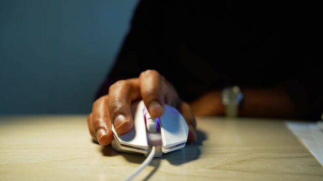 Hand using wired computer mouse on desk, Close view of a person&rsquo;s hand using a wired computer mouse on a wooden desk in a dark workspace
