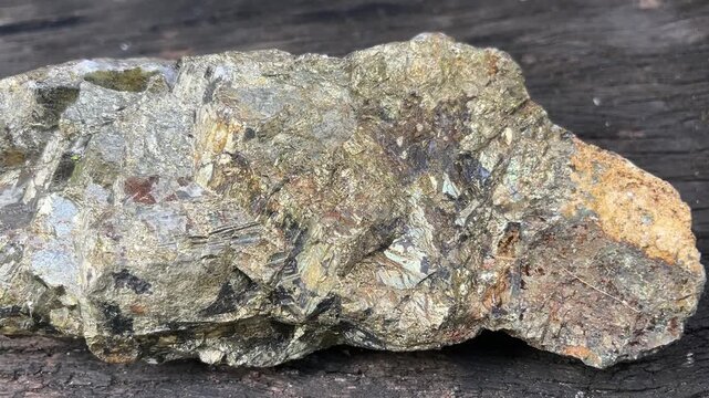 Pyrite Mineral Specimen: A detailed close-up showcases a rough, golden pyrite mineral specimen, revealing its cubic crystal structure and metallic luster, resting on a weathered wooden surface.