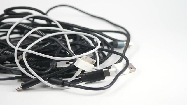Tangled pile of messy black and white charging cables on white background.