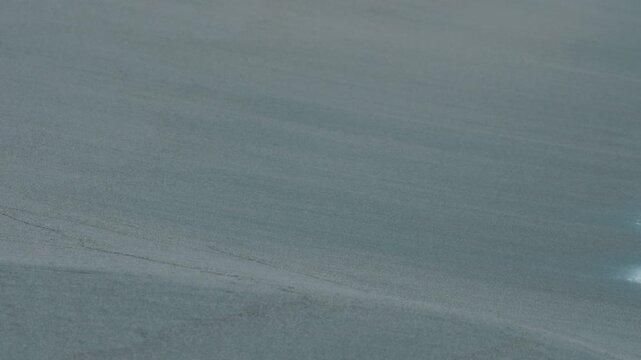Close-Up of Gentle Waves Washing Ashore on a Dark Blue Sandy Beach, Water Seeping into the Sand