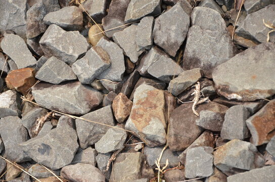 Close-up texture of rough grey and brown crushed rocks and gravel with scattered dry debris