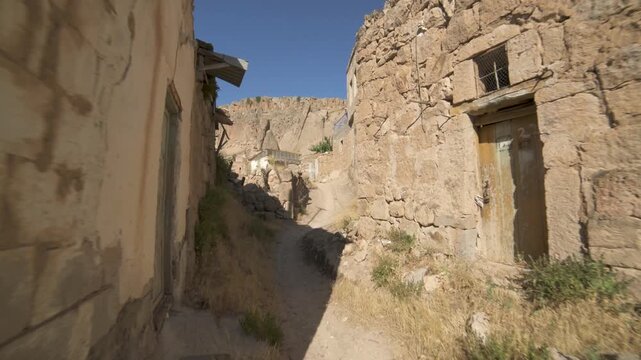 Narrow alley crosses abandoned Afghan village where empty houses stand along dusty path.