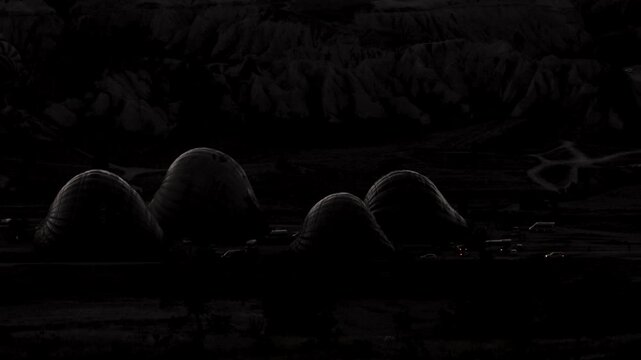 Hot air balloon inflation preparations begin at a dark launch site before sunrise.