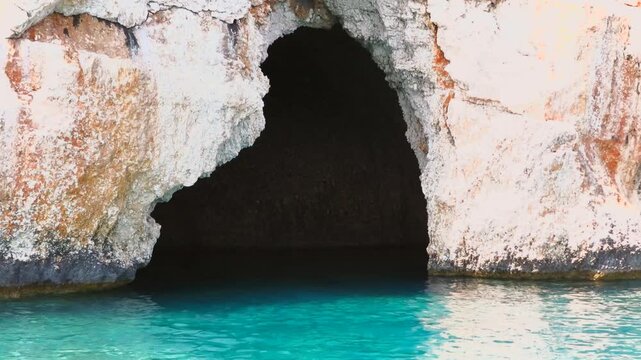 Natural sea cave entrance at water surface along rocky coastline, coastal geology landscape.