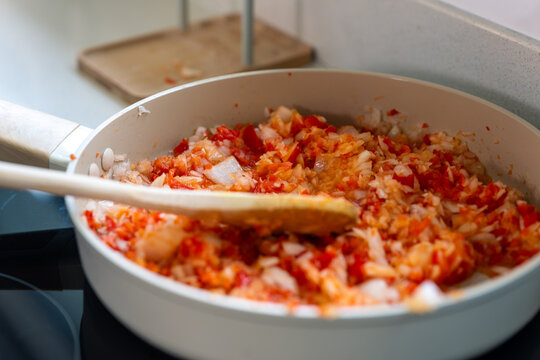 Stirring a fragrant sofrito of peppers and onions in a white pan