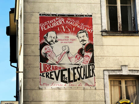 A banner for Librairie Le Reve de l'Escalier depicts Gustave Flaubert and Guy de Maupassant arm wrestling on a building facade - Rouen, France - September 5, 2026