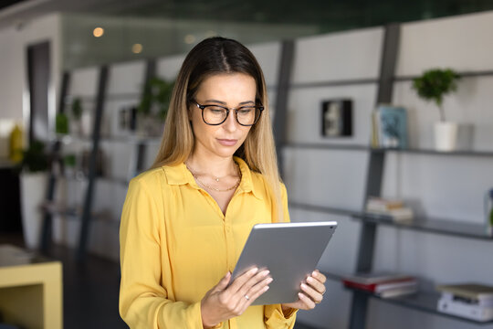 Young 30s businesswoman working online using modern digital tablet device in co-working office, focused in tasks completion, documents reviewing and presentation preparation. Productivity, workflow