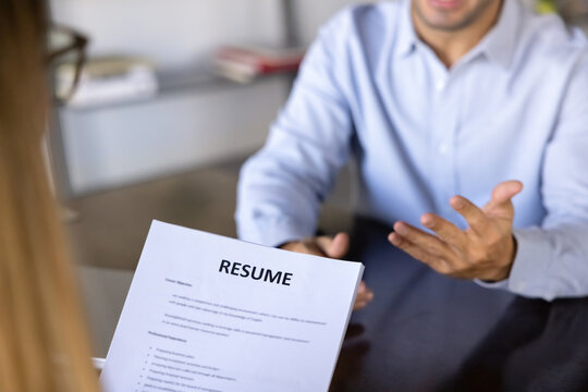 Close up focus on printed resume held by female HR manager during job interview, male applicant gestures while answers questions about experience, knowledge and qualifications. Recruitment process