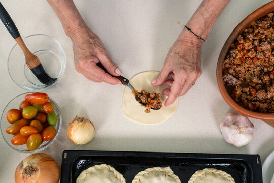 Carefully spooning savory meat filling onto fresh empanada dough