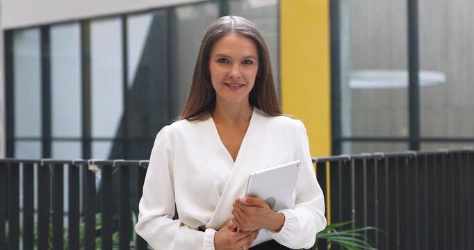 Smiling adult businesswoman posing for portrait with digital tablet on modern office balcony looking at camera conveying confidence professional competence career success female leadership empowerment